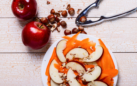 Fresh salad with apples, carrots, hazelnuts on a white wooden backgroundの写真素材