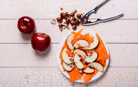Fresh salad with apples, carrots, hazelnuts on a white wooden backgroundの写真素材