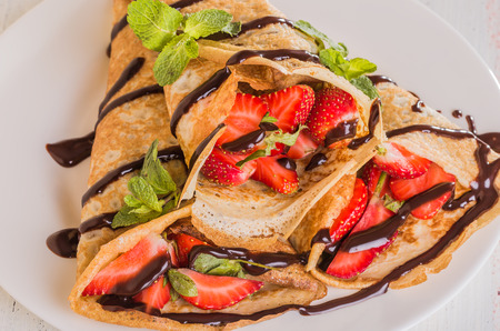 Homemade Crepes with strawberries and chocolate syrup on a white backgroundの写真素材