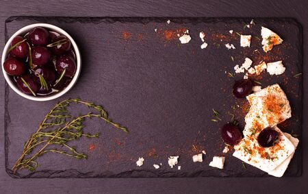 Food frame on dark stone background. Mediterranean olives in oil,feta cheese with paprika and thyme. Top view.の写真素材