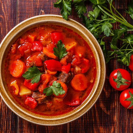 Goulash or stew in bowl served with parsley on wooden background, top view.の写真素材