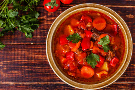 Goulash or stew in bowl served with parsley on wooden background, top view.の写真素材