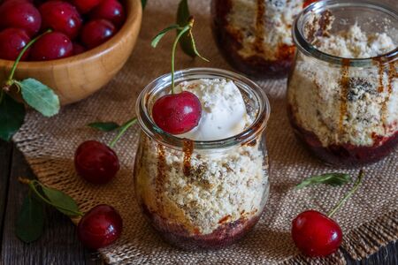 Homemade cherry crumble in glass jars on a dark wooden background, selective focus.の写真素材