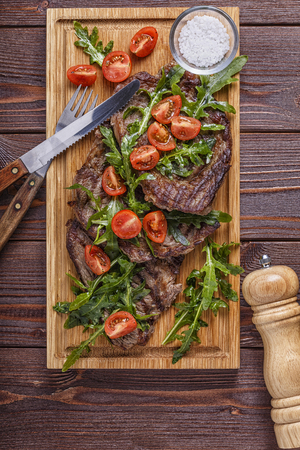 Steaks with arugula and tomatoes on dark wooden background, top view.の写真素材