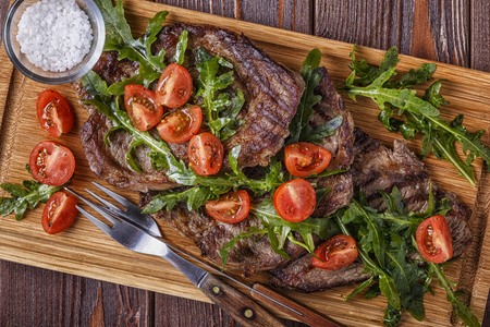Steaks with arugula and tomatoes on dark wooden background, top view.の写真素材