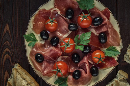 Plate with snack - prosciutto, jamon, ham, tomatoes, olives and baguette bread, top view.の写真素材