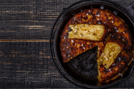 Spanish tortilla in a frying pan on dark wooden table, top view.の写真素材