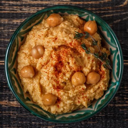Mashed chickpeas dip with tahini, lemon, garlic, olive oil, thyme and paprika on wooden table, top view.の写真素材