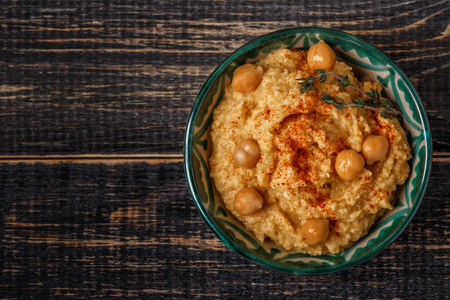 Mashed chickpeas dip with tahini, lemon, garlic, olive oil, thyme and paprika on wooden table, top view.の写真素材