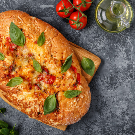 Focaccia with tomatoes, herbs and cheese, garnished with basil leaves.の写真素材