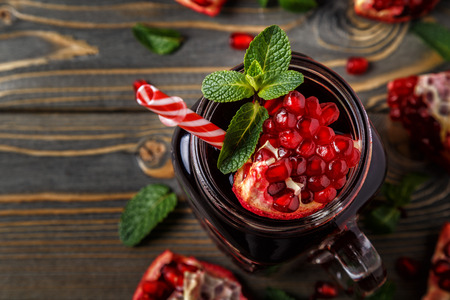 Glass of pomegranate juice with fresh pomegranate fruits and mint on wooden table, healthy drink concept.の写真素材
