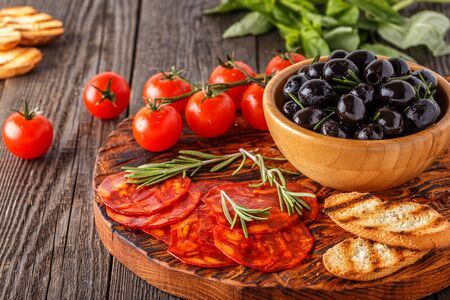 Spanish traditional chorizo sausage with fresh herbs, olives, tomatoes on a wooden board.の写真素材