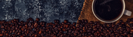 Coffee cup and coffee beans on dark background, top view.