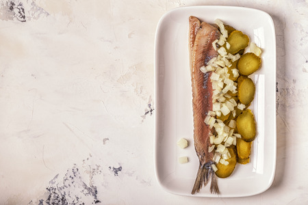 Traditional Dutch raw herring with onions and pickles on white background.