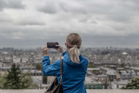 Woman tourist taking photo of the city in cloudy weather with mobile smart phone. camera.
