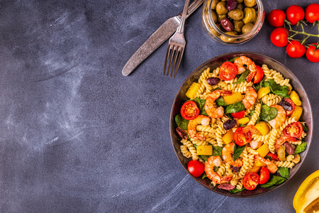 Fusili pasta salad with shrimps, tomatoes, peppers, spinach, olives, top view.の写真素材