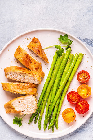 Roasted chicken breast with asparagus and tomatoes, top view.の写真素材