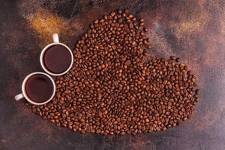 A cup of coffee and coffee beans poured in the form of a heart, top viewの写真素材