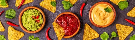 Mexican food background: guacamole, salsa, cheesy sauces with ingredients on black background, top...