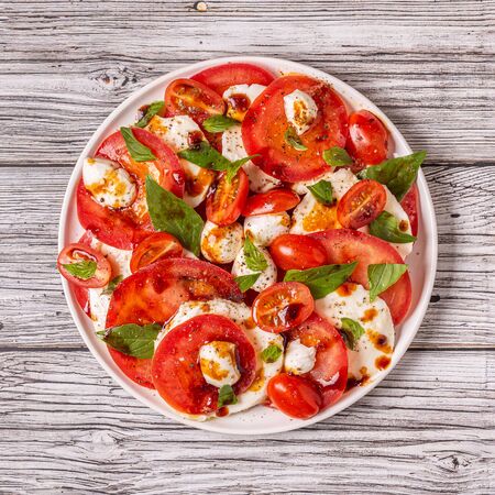 Italian caprese salad with sliced tomatoes, mozzarella cheese, basil, olive oil, balsamic vinegar. Top view, copy space.の写真素材