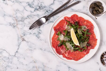 Marbled beef carpaccio with arugula, capers, lemon and parmesan cheese, top viewの写真素材