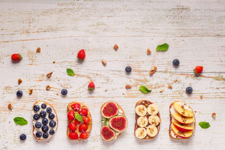 Homemade summer toast with cream cheese, nut butter and fruits and berries, top view.