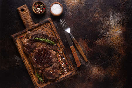 Grilled beef steak with spices on a wooden board, top view.