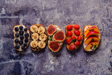Homemade summer toast with cream cheese, nut butter and fruits and berries, top view.