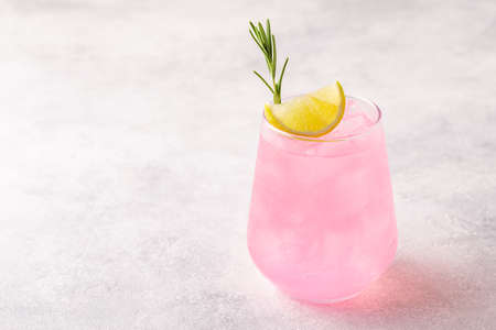 Refreshing pink drink or cocktail with ice, garnished with a slice of lime and rosemary.の写真素材