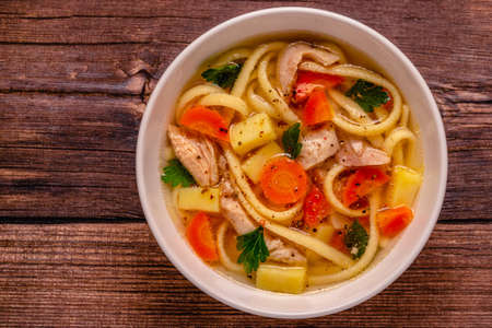 Chicken soup with noodles and vegetables in white bowlの写真素材