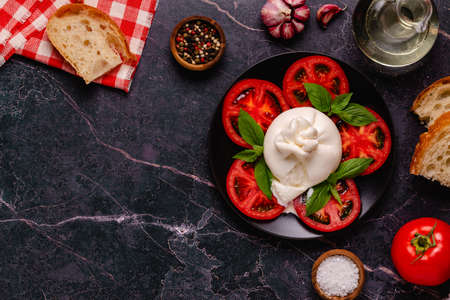 Caprese salad with tomatoes, burrata cheese and basil. dark background. top view.