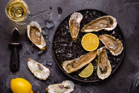 Opened fresh oysters on a plate, served with lemon and ice, top view.