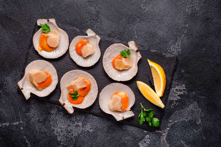 Raw scallops with lemon parsley on a black stone plateの写真素材