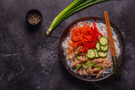 Bowl of rice noodles with vegan soy meat and vegetables on dark background, top viewの写真素材