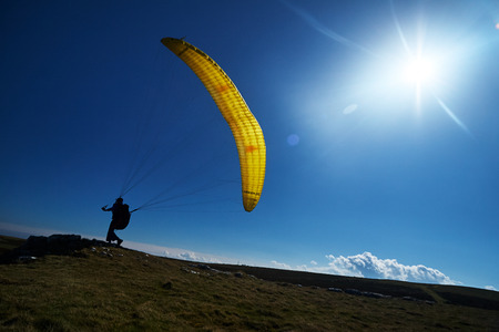 Paragliders on a mountain top preparing to take flight flying over a mountain valley in summerの写真素材