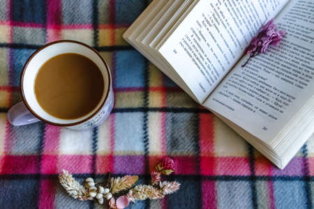 Coffe mug with flowers and opened book on a plaid