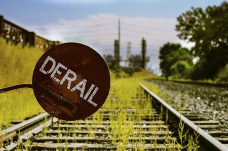 Derailer sign over train tracks with green grass and industrial complex in backgroundの写真素材