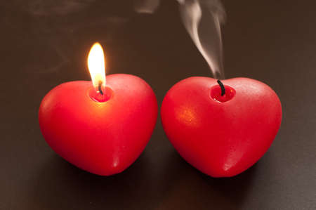 Two candles in the shape of a heart and one is lit and burns, and the other is extinguished and there is smokeの写真素材