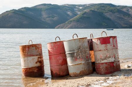 Five rusty fuel and chemical drums on the beach of a lakeの写真素材