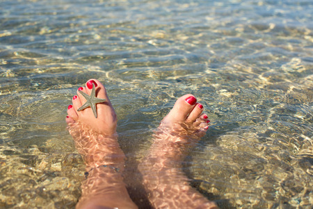 Female feet in a see water with starfishの写真素材