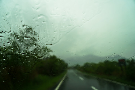 View of blurred road way and mountain view with raindrop on car windscreen while driving through local road on rainy day in Yufuin, Japanの写真素材