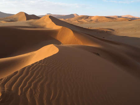 Natural curved ridge line and wind blow pattern of rusty red sand dune with shade and shadow on vast desert landscape background, Sossus, Namib desert, Namibiaの写真素材