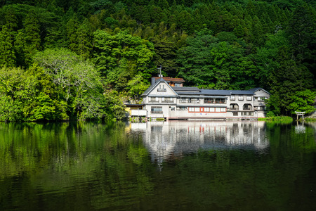 Beautiful abundant natural green mountain plant reflection on fresh lake Kinrin with buildings during springtime, Yufuin, Japanのeditorial素材