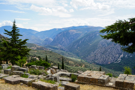 Panoramic view of ancient ruin at temple of Delphi with green olive groves valley, Parnassus mountain and blue sky background, Delphi, Greeceの写真素材