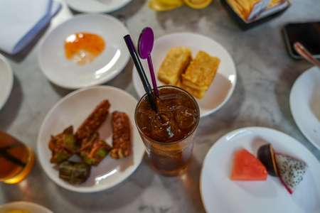 Sweet and sour cold  ice lemon tea with ice tube among afternoon tea snack, dessert and fresh fruit for refreshment on marble table top, Penang, Malaysiaの写真素材
