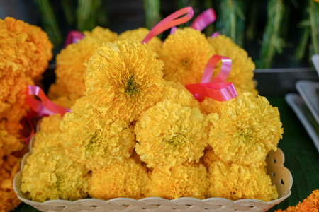 Fresh Thai style flower garlands made of bright yellow marigold with pink ribbon selling on basket in local market, Thailandの写真素材