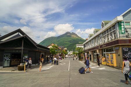 Yufuin, Japan - May 13, 2017 : Main road from train station filled with tourists, streetscape and local shops direct to fresh green Yufudake mountain peak and blue sky background view, Yufuin, Kyushuのeditorial素材