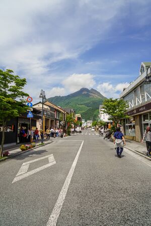 Yufuin, Japan - May 13, 2017 : Main road from train station filled with people, streetscape and shops direct to fresh green Yufudake mountain peak, blue sky and white cloud background, Yufuin, Kyushuのeditorial素材