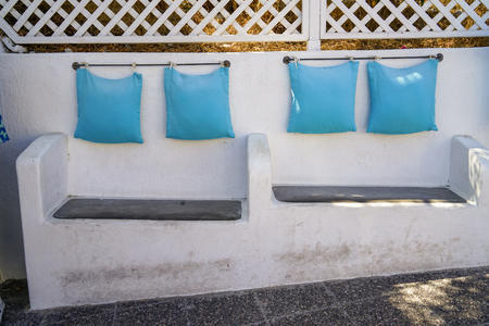 Solid built-in white concrete custom design bench seat chair with light blue pillow hanging by steel rod along island walkway, Santorini, Greeceの写真素材
