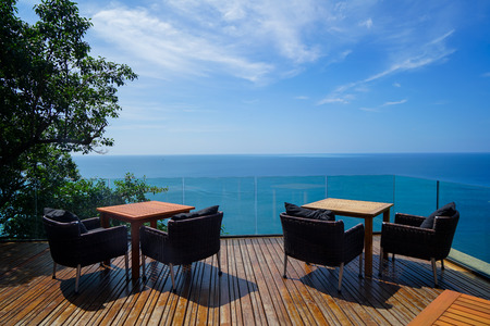 Tables and rattan outdoor armchairs setting on wooden deck and glass balcony with panoramic Andaman...